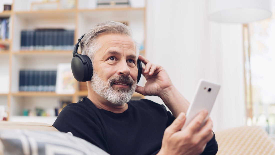 Älterer Mann hört mit Kopfhörern Musik und schaut entspannt auf sein Smartphone als Symbol für aktives und gesundes Altern.