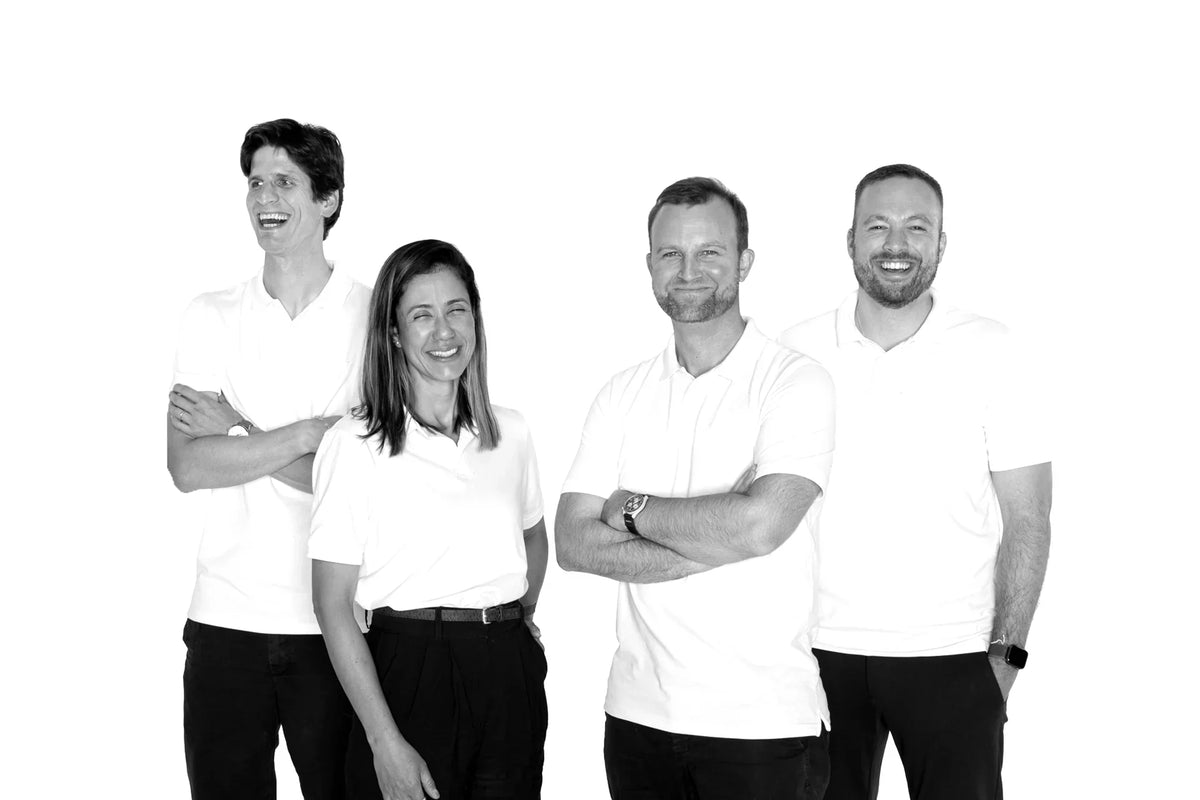 Lächelndes Team in weißen Poloshirts und schwarzer Hose vor weißem Hintergrund